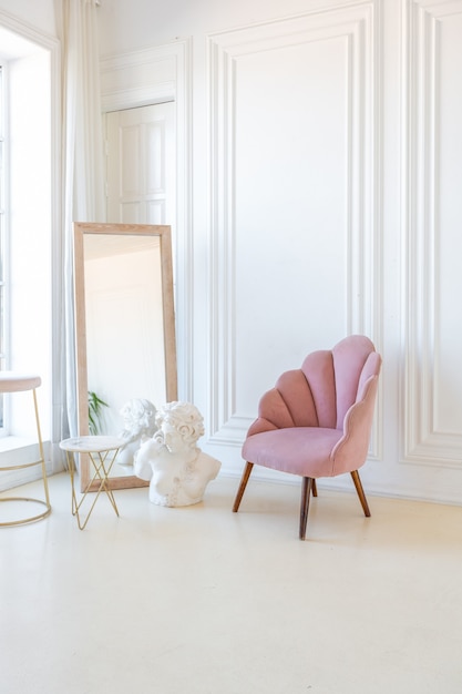 Intérieur lumineux délicat et confortable du salon avec un mobilier moderne et élégant de couleur rose pastel et des murs blancs avec des moulures en stuc à la lumière du jour