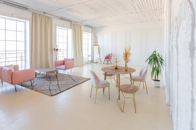 Intérieur lumineux délicat et confortable du salon avec un mobilier moderne et élégant de couleur rose pastel et des murs blancs avec des moulures en stuc à la lumière du jour