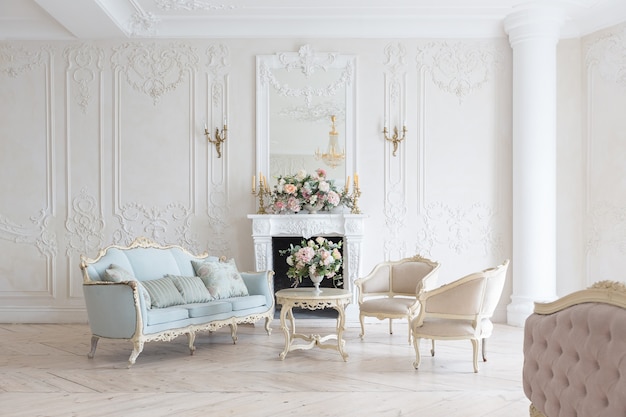 Intérieur lumineux luxueux dans le style baroque. Une chambre spacieuse avec un beau mobilier de rue chic, une cheminée et des fleurs. stuc végétal sur les murs et parquet en bois clair
