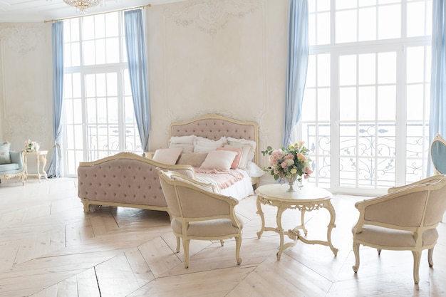 Intérieur lumineux luxueux dans le style baroque. Une chambre spacieuse avec un beau mobilier de rue chic, une cheminée et des fleurs. stuc végétal sur les murs et parquet en bois clair