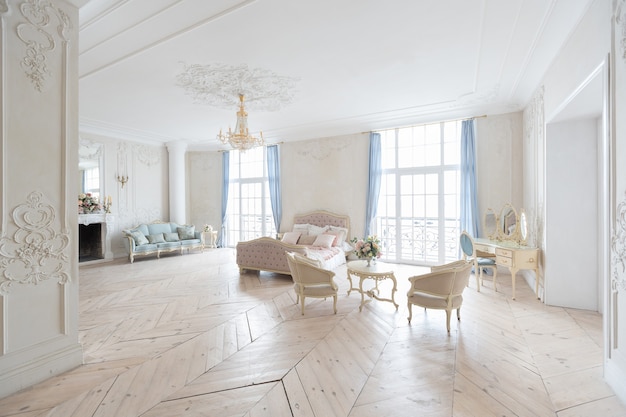 Intérieur lumineux luxueux dans le style baroque. Une chambre spacieuse avec un beau mobilier de rue chic, une cheminée et des fleurs. stuc végétal sur les murs et parquet en bois clair