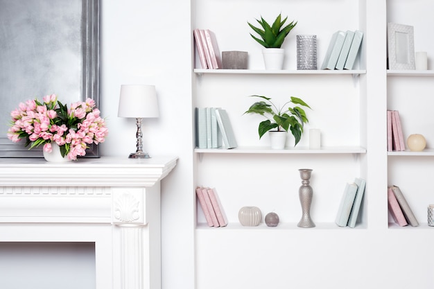 Intérieur de luxe lumineux avec cheminée et fleurs. Étagères avec des livres et des décorations