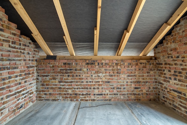 Intérieur de maison en brique inachevée avec sol en béton, murs nus prêts pour le plâtrage et toiture en bois