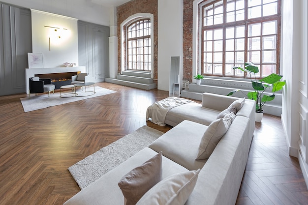 Intérieur minimaliste d'un appartement décloisonné ultra moderne avec des murs blancs et gris avec des meubles rembourrés élégants en relief et gris et d'immenses fenêtres