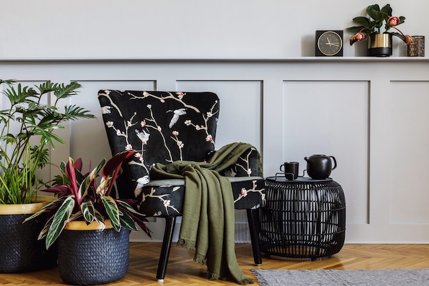 Intérieur moderne du salon avec fauteuil design, boiseries avec étagère, beaucoup de plantes, table basse, mur gris, décoration, tapis et accessoires personnels dans la décoration intérieure.