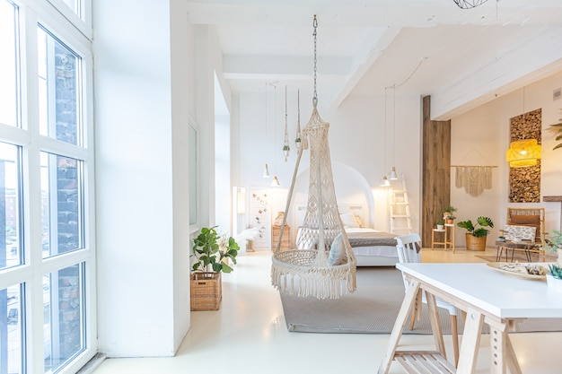 Intérieur moderne à la mode d'un studio lumineux avec des colonnes en bois de style loft, décoré de briques, de marbre et de bois avec des meubles élégants et des murs blancs