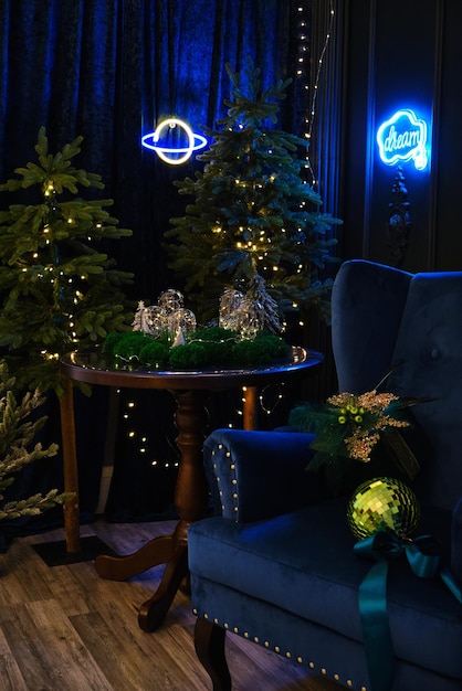 Intérieur de Noël bleu et vert. Un intérieur féerique avec un mur vert, un fauteuil bleu, une table ronde sur laquelle il y a des ampoules incandescentes décorées de mousse et des arbres de Noël avec des lumières et des enseignes au néon