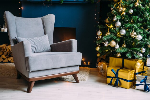 Intérieur de Noël. Mur bleu avec chaise. Arbre de Noël élégant avec des cadeaux d'or et d'argent.