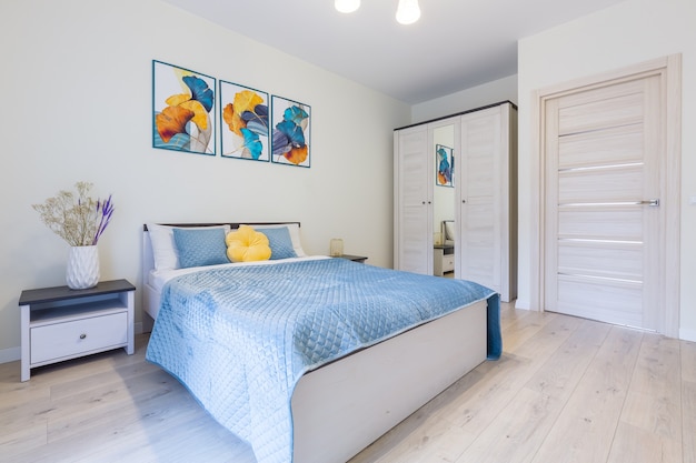 Photo intérieur d'une petite chambre dans un style minimaliste moderne, dans des couleurs claires, un grand lit avec une couverture bleue