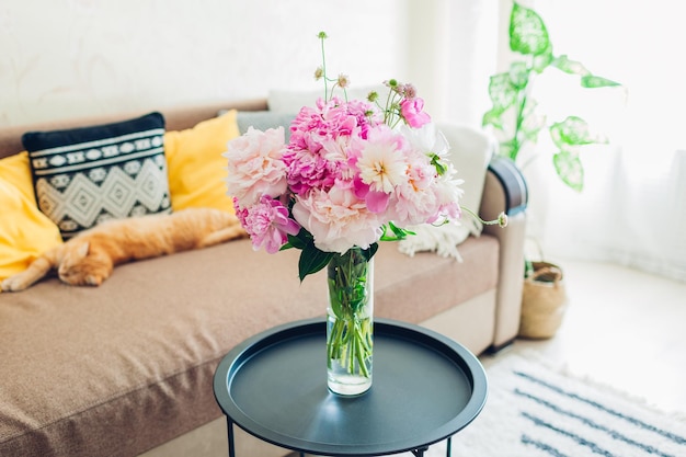 Intérieur plat du salon décoré d'un bouquet de plantes de panier de pivoines et d'un tapis de couchage pour chat