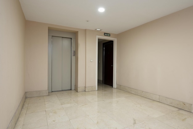Intérieur d'un portail résidentiel avec ascenseur avec portes en métal gris et sols en marbre crème poli