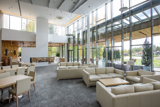 Intérieur d'un restaurant confortable à l'intérieur d'un grand centre d'affaires avec plusieurs tables entourées de chaises et de canapés en cuir blanc doux pour le repos