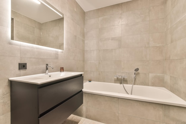 L'intérieur de la salle de bain avec un lavabo encastré dans le meuble sous le miroir et la baignoire entourée de carrelage