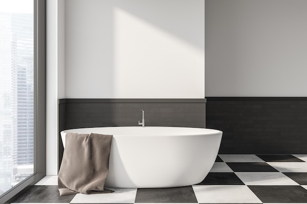 L'intérieur d'une salle de bain moderne avec des murs blancs et gris, un sol carrelé, une fenêtre de grenier et confortable avec une baignoire avec une serviette grise accrochée.
