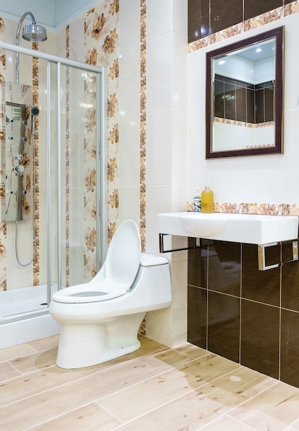 Intérieur de la salle de bain avec murs blancs, cabine de douche avec paroi vitrée, toilettes et lavabo