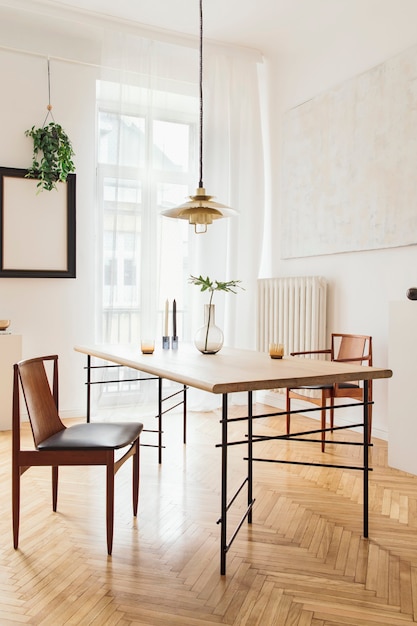 Intérieur de salle à manger élégant et moderne avec table de partage design, chaises, suspension dorée, peintures abstraites et accessoires élégants. Feuilles tropicales dans un vase. Décoration d'intérieur éclectique.