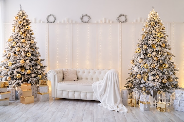 Intérieur de salon blanc avec des arbres du nouvel an décorés de coffrets cadeaux et d'un canapé moderne de couleur dorée