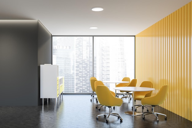 L'intérieur d'un salon élégant avec des murs gris et jaunes, un sol en béton, des chaises jaunes près de tables rondes et des armoires blanches.