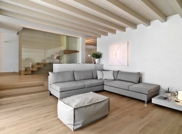 Intérieur de salon moderne avec parquet et plafond en bois au premier plan les canapés gris avec un repose-pieds à l'arrière-plan l'escalier