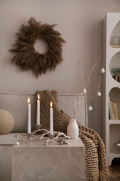 Photo intérieur de salon de noël domestique et confortable avec canapé en velours côtelé, étagère blanche, chandelier avec bougie, décoration de vêtements de noël, cadeaux et accessoires décoration d'intérieur modèle de temps en famille