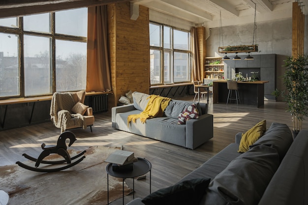 Intérieur de style loft sombre d'une grande maison de campagne confortable. appartement décloisonné avec coin cuisine, zone de repos et coin chambre. Immenses fenêtres et décoration en bois