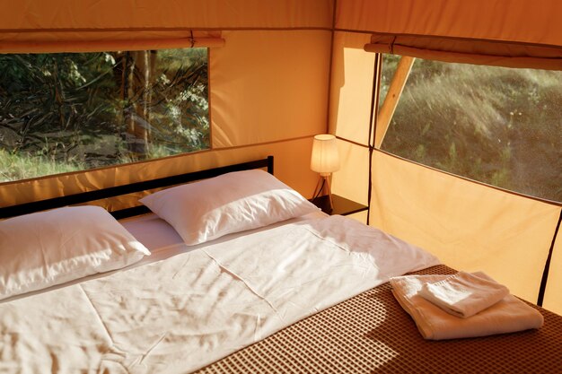 Intérieur de la tente de glamping ouverte confortable avec lumière à l'intérieur pendant le coucher du soleil Tente de camping de luxe pour les vacances d'été en plein air et les vacances Concept de style de vie