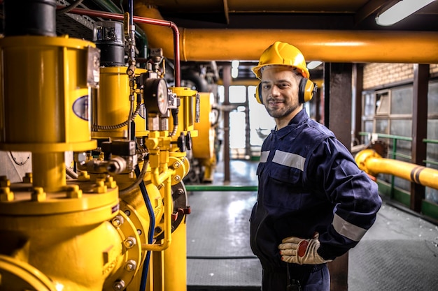 Intérieur de l'usine de chauffage urbain et technicien expérimenté debout près de la source d'énergie du gazoduc