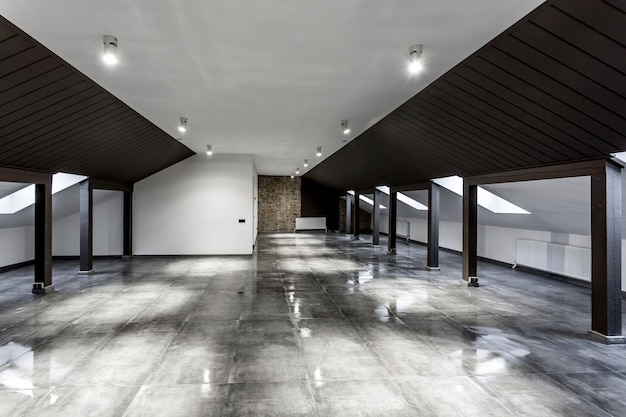 Intérieur vide de la chambre mansardée loft non meublé avec colonnes en bois et sol en béton humide au niveau du toit en couleur de style noir et blanc