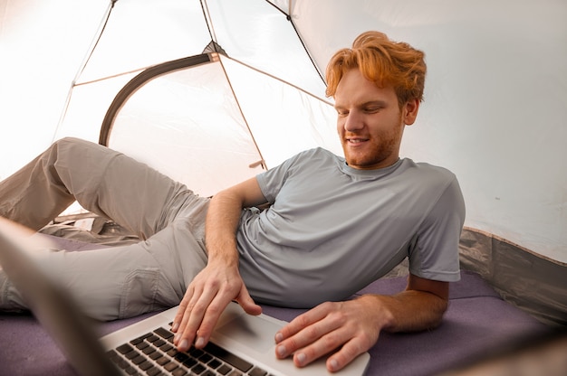 Sur Internet. Un jeune homme allongé dans une tente avec un ordinateur portable