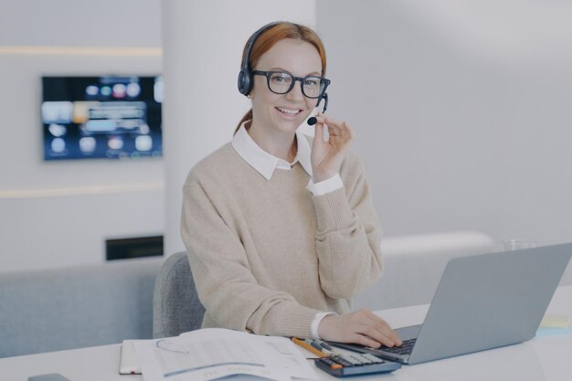 Interprète en ligne Une jeune femme heureuse dans un casque parle au client devant un ordinateur portable