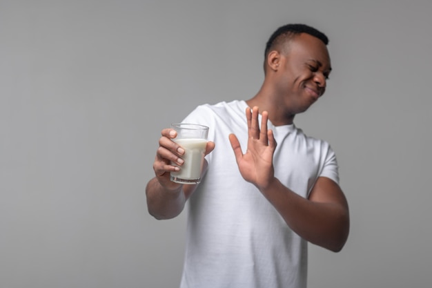 Intolérance au lactose. Jeune homme noir adulte avec grimace refusant le verre de lait faisant des gestes en se tenant debout en studio