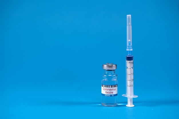 Invention du vaccin contre le coronavirus covid-19 dans un flacon de médicament en verre, seringue pour injection sur bleu