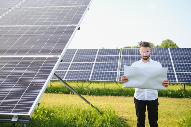 Investisseur masculin barbu positif debout contre des panneaux photovoltaïques produisant de l'énergie alternative