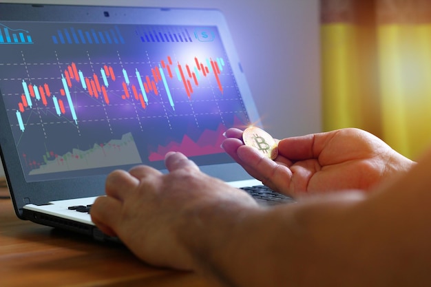 Un investisseur de pièces de monnaie tenant une pièce de monnaie dans la main suit la valeur de la pièce de monnaie sur un ordinateur portable