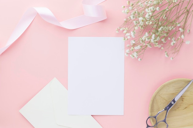 Invitation de carte de voeux vierge maquette 5x7 sur enveloppe avec fleurs de gypsophile et ruban sur fond de papier pastel rose maquette à plat