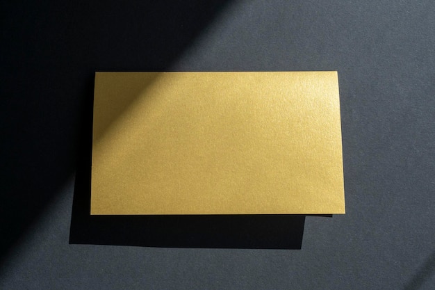 Photo invitation de maquette de carte de visite dorée sur une surface noire avec ombres et lumière du soleil