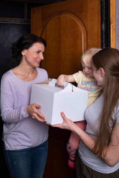 Photo les invités souriants reçoivent une grande boîte avec un gâteau. la jeune mère et l'enfant accueillent un invité avec un cadeau.