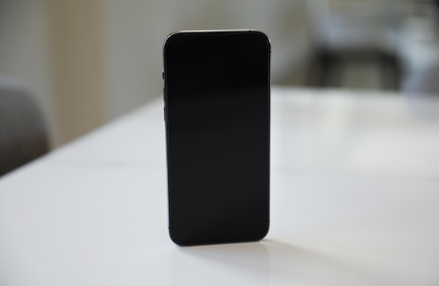 Un iphone noir est posé sur une table blanche.