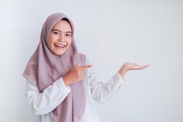 L'islam asiatique femme musulmane portant le foulard pointe le doigt vers l'espace de copie vierge zone de visage de sourire Femme indonésienne Concept de religion isolé sur fond gris