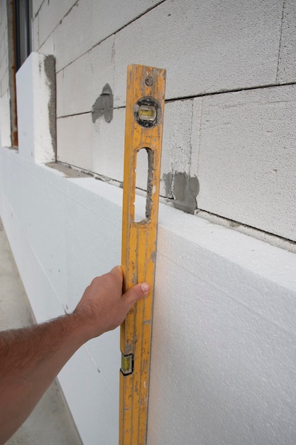 Isolation thermique. Main de travailleur avec une feuille de mousse de polyuréthane rigide blanche de mesure de niveau sur le mur