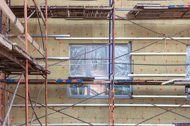 Isolation thermique d'une maison en brique rouge avec de la laine minérale. L'utilisation d'échafaudages lors de la construction d'une maison.