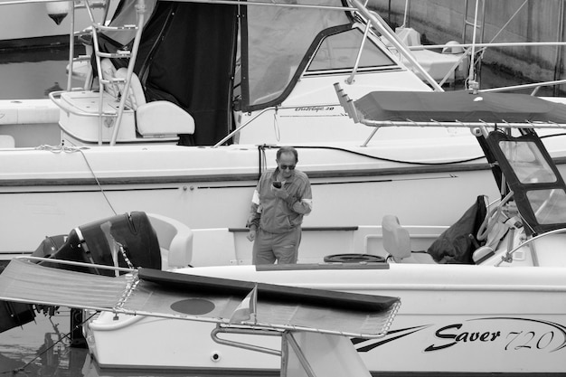 Photo italie, sicile, mer méditerranée, marina di ragusa (province de ragusa); 22 mai 2023, homme sur un bateau à moteur dans le port - réditorial