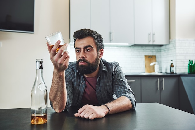 L'ivresse n'est rien d'autre que la folie volontaire homme ivre avec verre et bouteille de whisky assis