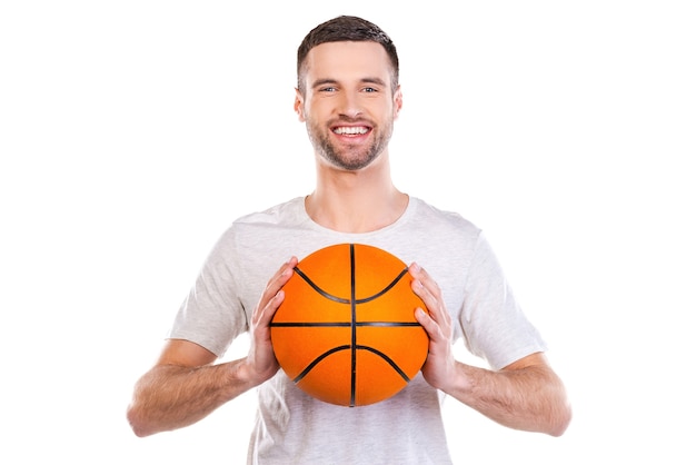 J'adore le basket. Jeune homme confiant tenant un ballon de basket et souriant en se tenant debout sur fond blanc