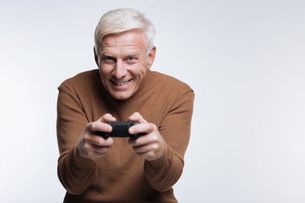 J'adore le jeu. Cheerful senior man jouant à un jeu vidéo et souriant sur fond gris