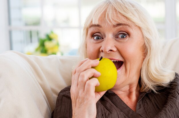 J'adore les pommes! Cheerful senior woman holding apple et regardant la caméra alors qu'il était assis à la chaise