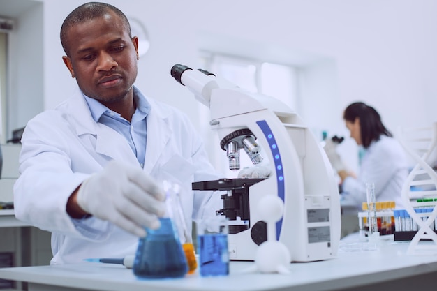 J'adore la science. Biologiste professionnel sérieux travaillant avec son microscope et son collègue travaillant en arrière-plan