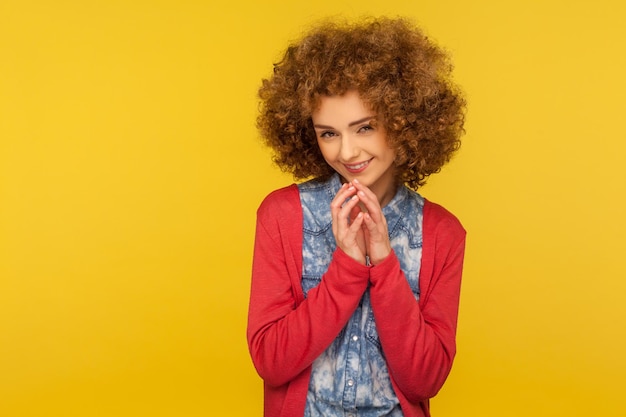 J'ai un plan délicat Portrait d'une femme rusée et sournoise avec des cheveux bouclés moelleux serrant les mains et souriant mystérieusement intrigant trompe mal farce studio intérieur tourné isolé sur fond jaune