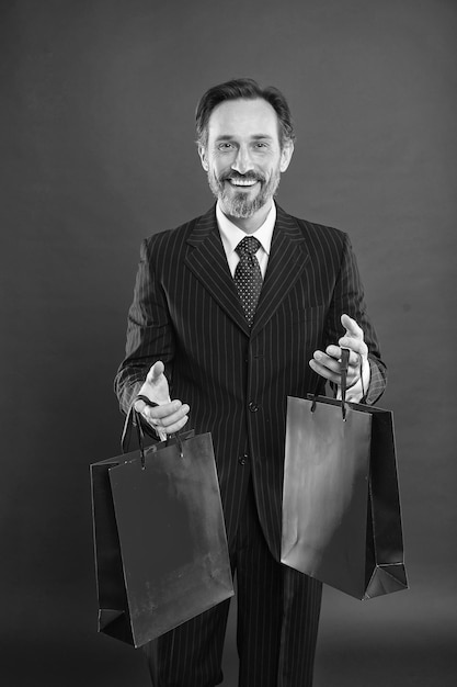 J'aide l'économie Je fais beaucoup de shopping Heureux shopper fond rouge Homme d'affaires tient des sacs à provisions Homme mûr aime faire du shopping