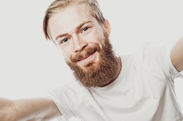 J'aime l'homme barbu selfie tenant un smartphone et faisant selfie et souriant en se tenant debout sur fond blanc